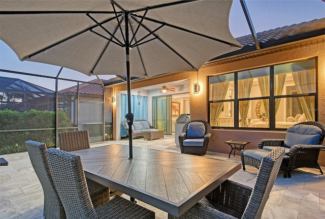 patio terrace at dusk featuring ceiling fan and glass enclosure