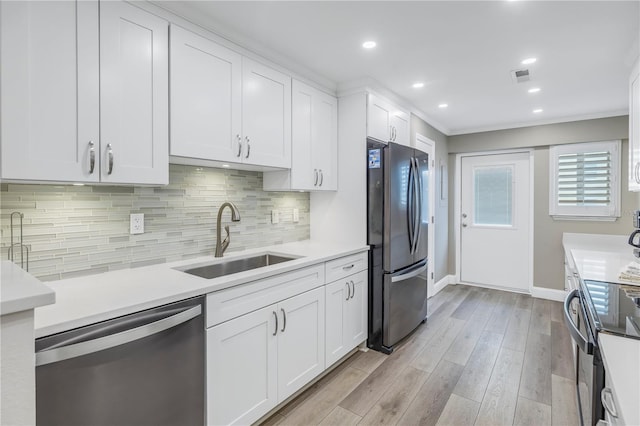 kitchen with appliances with stainless steel finishes, light hardwood / wood-style floors, tasteful backsplash, white cabinets, and sink