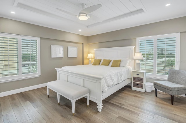 bedroom with ceiling fan, a tray ceiling, and light hardwood / wood-style flooring