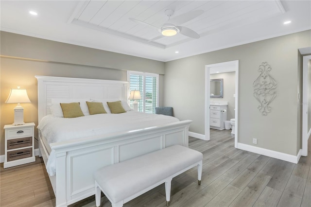 bedroom with light wood-type flooring, a raised ceiling, connected bathroom, and ceiling fan