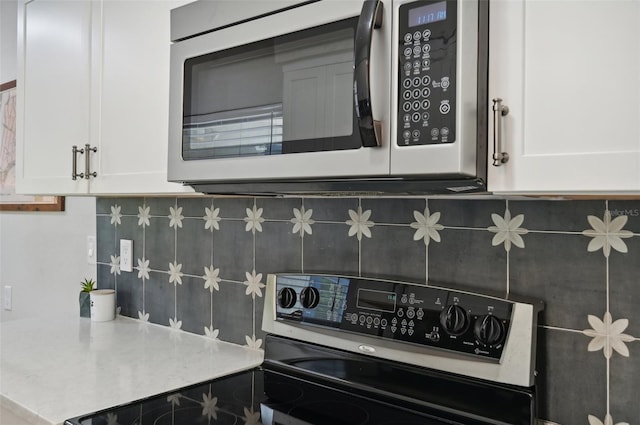 kitchen featuring decorative backsplash, stove, and white cabinetry