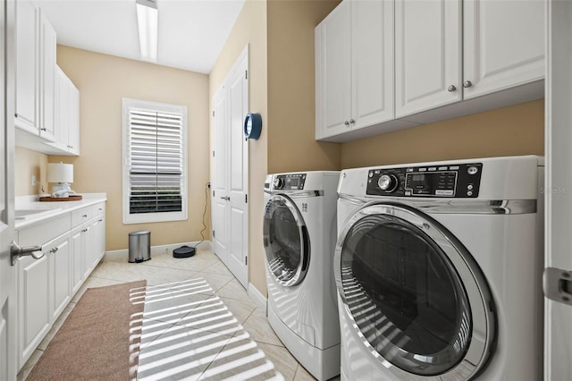 clothes washing area with washing machine and dryer, light tile patterned floors, and cabinets