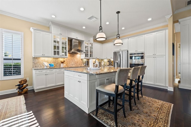 kitchen with a breakfast bar, light stone counters, an island with sink, wall chimney range hood, and stainless steel appliances