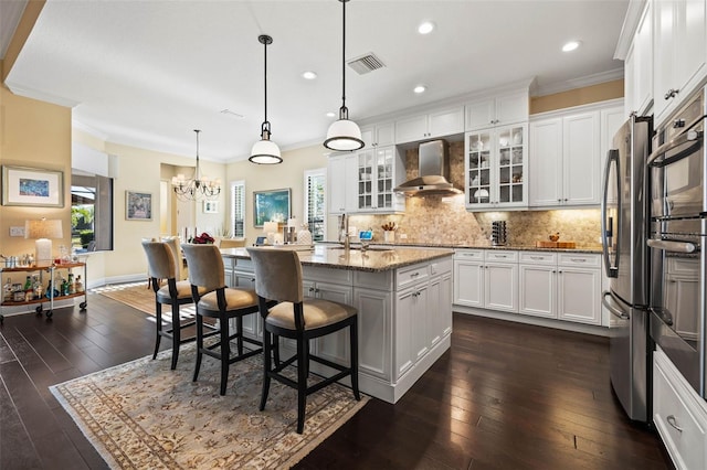 kitchen featuring an island with sink, white cabinets, decorative light fixtures, and wall chimney range hood