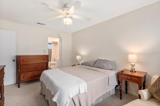 bedroom with ceiling fan, light colored carpet, and ensuite bath