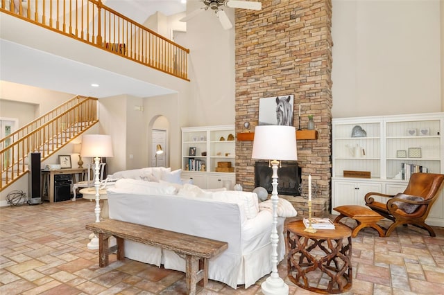 living room featuring a stone fireplace, a towering ceiling, and ceiling fan