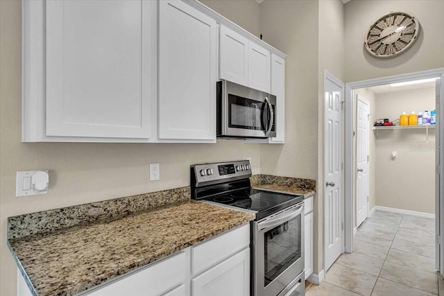 kitchen with dark stone countertops, light tile patterned floors, stainless steel appliances, and white cabinets