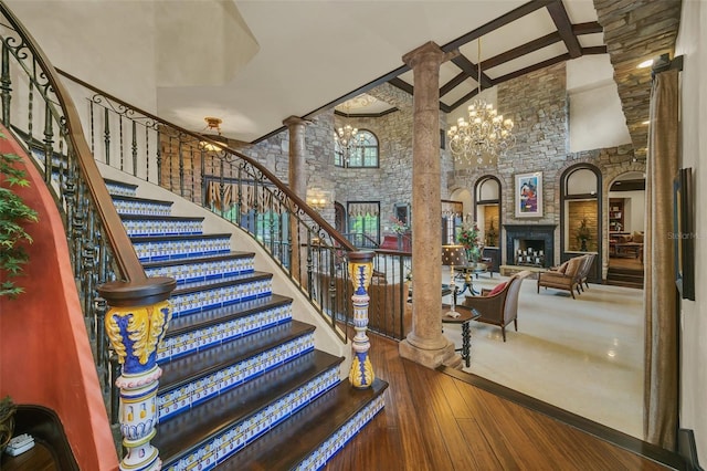 staircase with high vaulted ceiling, hardwood / wood-style floors, a fireplace, and ornate columns