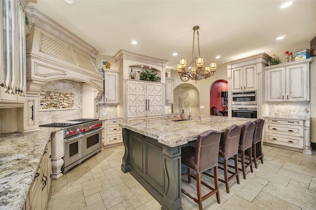 kitchen with light stone counters, pendant lighting, a kitchen island with sink, appliances with stainless steel finishes, and a kitchen breakfast bar