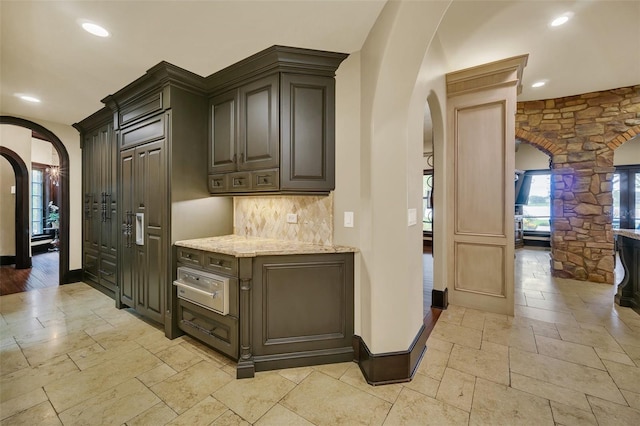 kitchen featuring dark brown cabinets, light stone counters, and tasteful backsplash