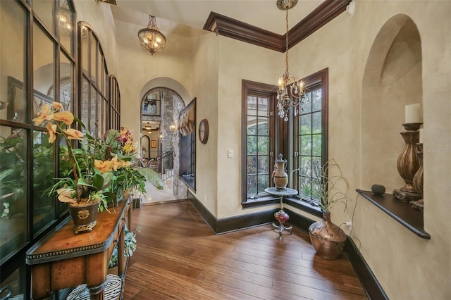 entryway featuring ornamental molding, a towering ceiling, a chandelier, and dark wood-type flooring