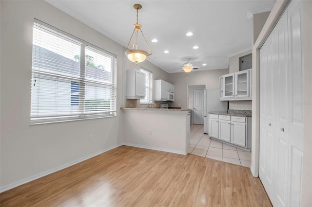 kitchen with ceiling fan, kitchen peninsula, decorative light fixtures, white cabinets, and light wood-type flooring