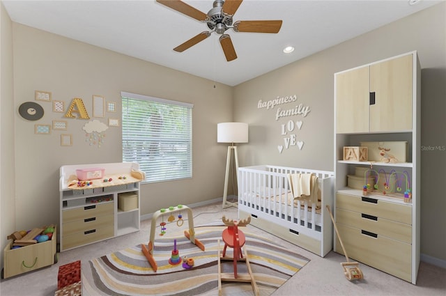 carpeted bedroom featuring ceiling fan and a nursery area