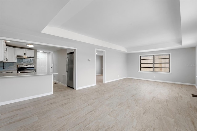 unfurnished living room featuring a raised ceiling and sink