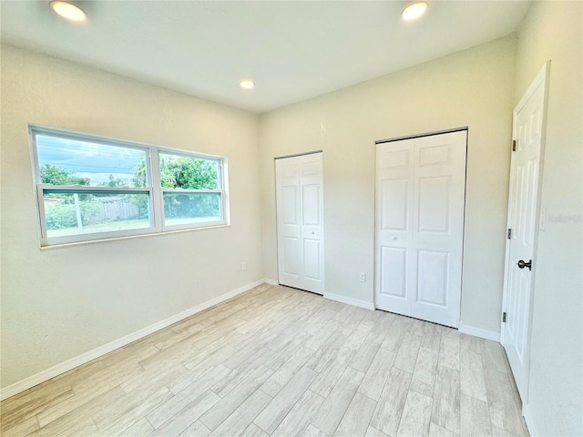 unfurnished bedroom featuring light hardwood / wood-style flooring and two closets