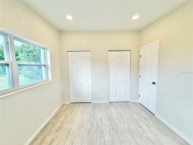 unfurnished bedroom featuring multiple closets and light hardwood / wood-style flooring