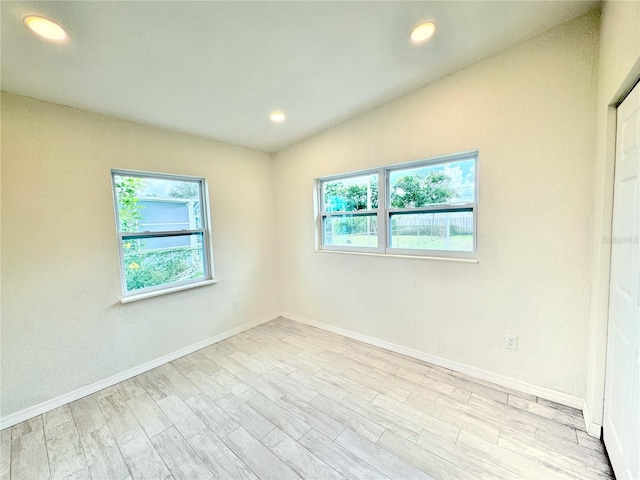 empty room featuring light wood-type flooring, vaulted ceiling, and a healthy amount of sunlight