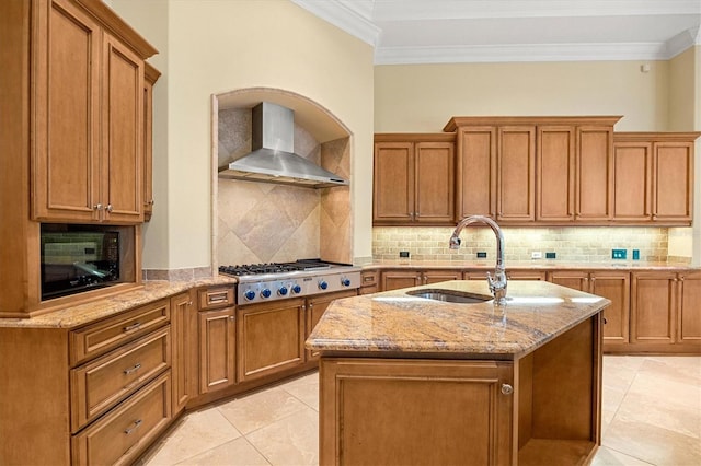 kitchen with decorative backsplash, stainless steel gas cooktop, a center island with sink, and wall chimney range hood