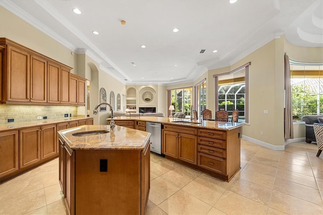 kitchen with light stone counters, sink, stainless steel dishwasher, and a large island with sink