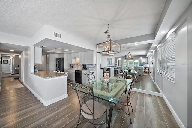 dining area featuring an inviting chandelier, a textured ceiling, sink, and dark wood-type flooring