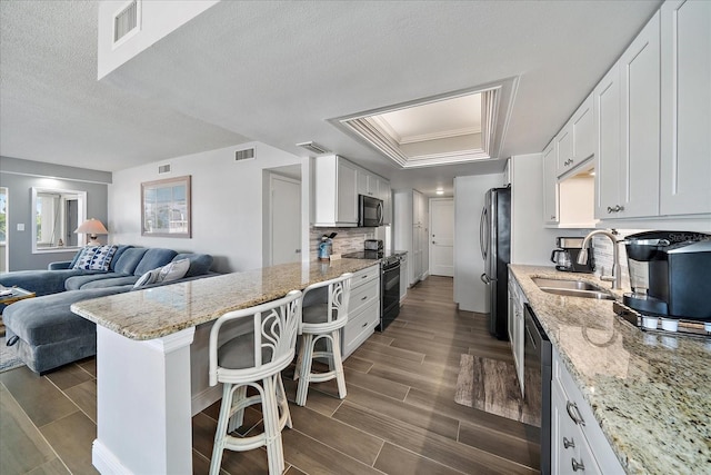 kitchen featuring a kitchen breakfast bar, white cabinetry, a raised ceiling, black appliances, and sink