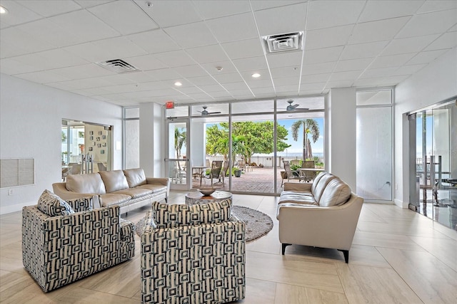 living room featuring ceiling fan, a wall of windows, and a drop ceiling