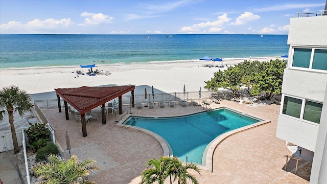 view of pool featuring a water view, a beach view, and a patio area