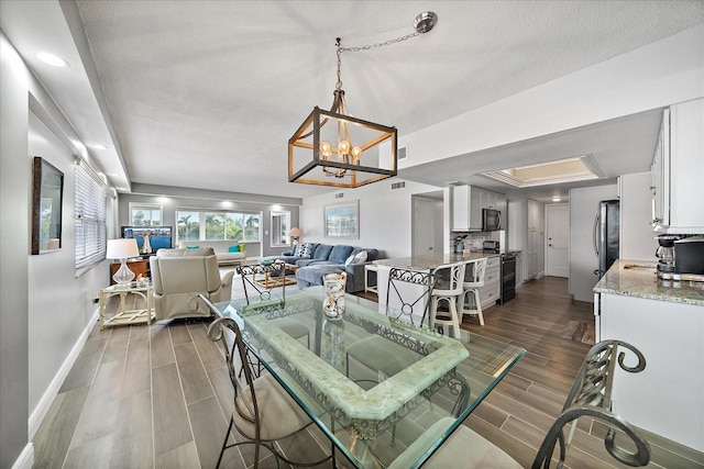 dining space with an inviting chandelier, a textured ceiling, a raised ceiling, and dark hardwood / wood-style flooring