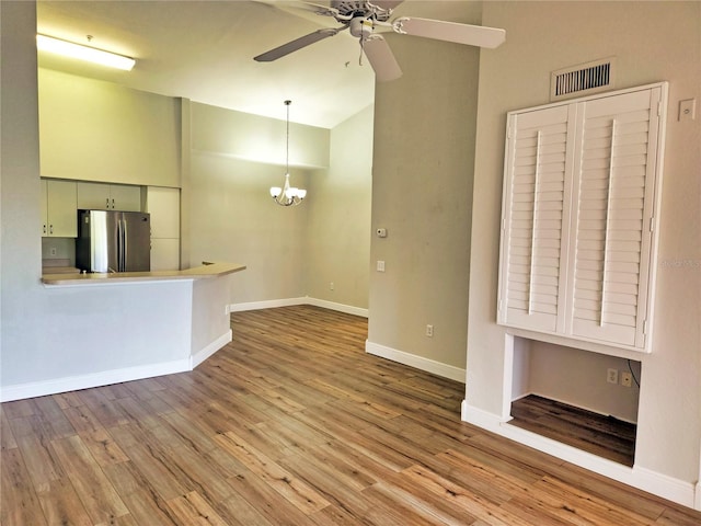 unfurnished living room with ceiling fan with notable chandelier and light hardwood / wood-style flooring