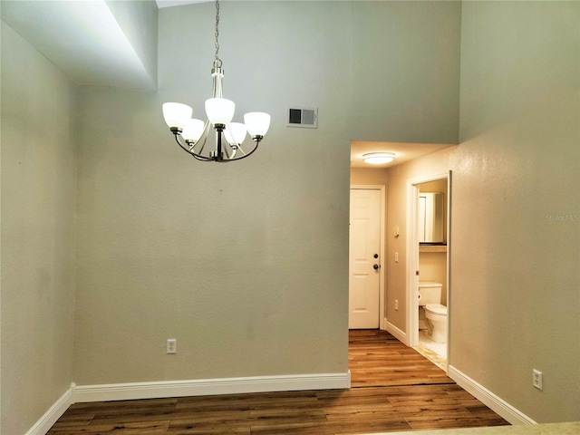 spare room featuring wood-type flooring, a chandelier, and a high ceiling