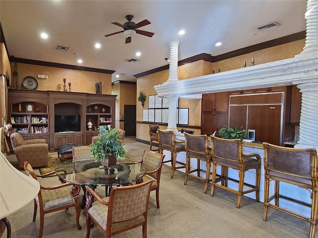 carpeted dining room with ceiling fan, crown molding, and ornate columns