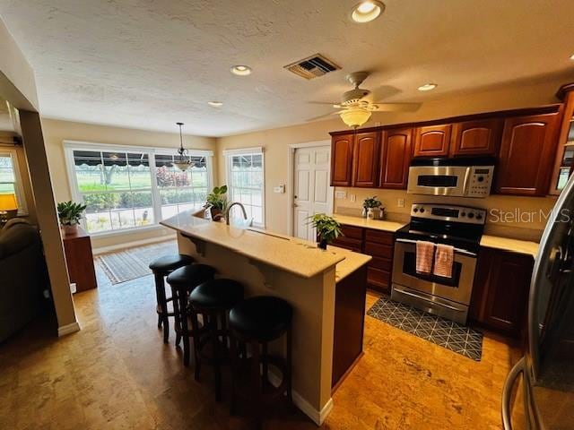 kitchen featuring decorative light fixtures, ceiling fan, an island with sink, a kitchen breakfast bar, and stainless steel range with electric stovetop