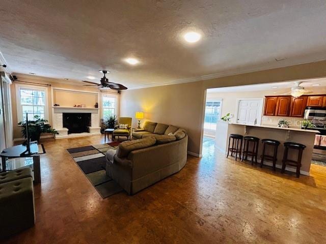 living room featuring ceiling fan, a textured ceiling, crown molding, and a fireplace