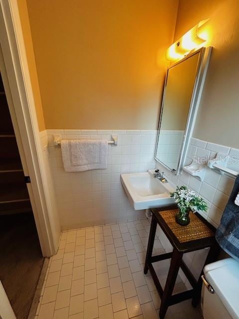 bathroom featuring toilet, tile patterned flooring, tile walls, and sink