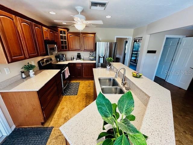 kitchen with ceiling fan, appliances with stainless steel finishes, an island with sink, and sink