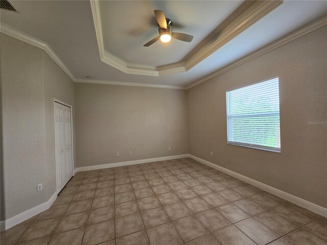 unfurnished room with ceiling fan, a tray ceiling, crown molding, and light tile patterned floors