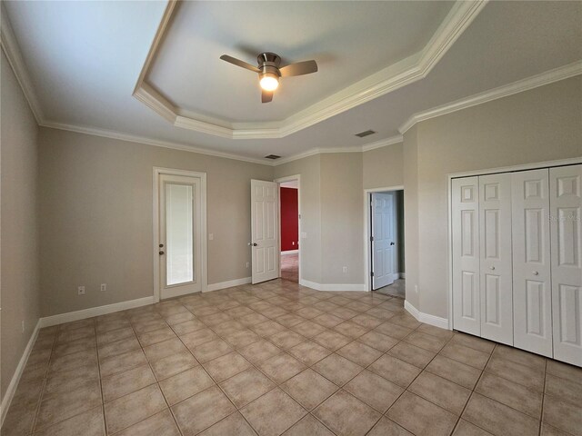 unfurnished bedroom featuring light tile patterned floors, a closet, crown molding, a tray ceiling, and ceiling fan