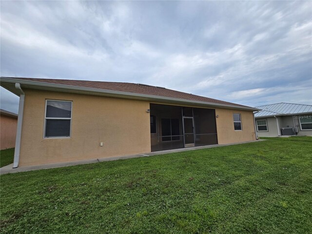 back of property with a sunroom, a lawn, and central AC