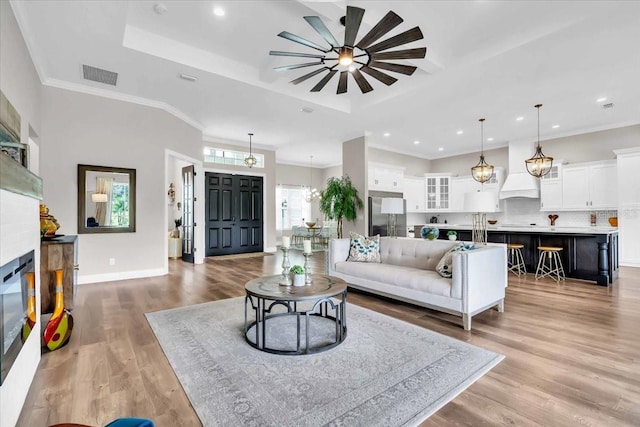 living room with ornamental molding, light hardwood / wood-style floors, a raised ceiling, and ceiling fan with notable chandelier