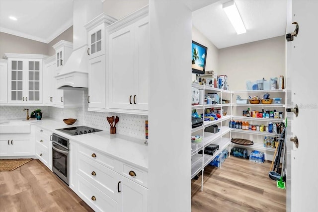 kitchen featuring oven, white cabinetry, black electric cooktop, light hardwood / wood-style floors, and decorative backsplash