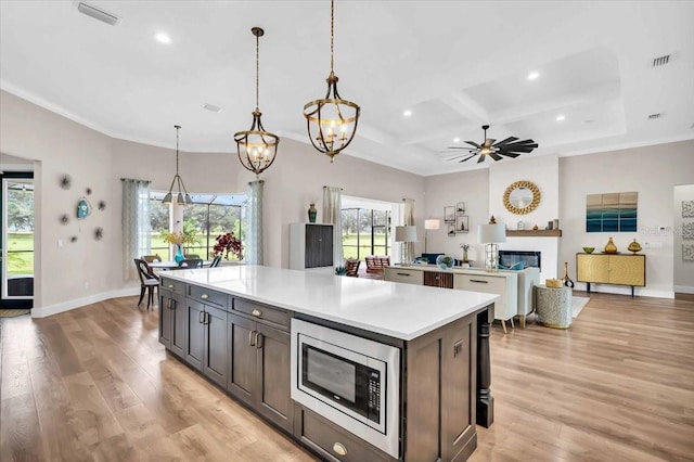 kitchen with light wood-type flooring, decorative light fixtures, coffered ceiling, ceiling fan with notable chandelier, and stainless steel microwave