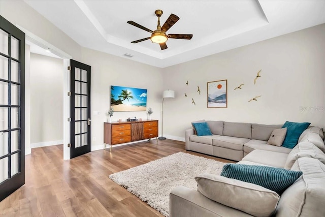 living room featuring light wood-type flooring, a raised ceiling, ceiling fan, and french doors