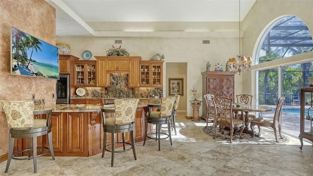 kitchen with a kitchen breakfast bar, an inviting chandelier, backsplash, light stone countertops, and stainless steel fridge