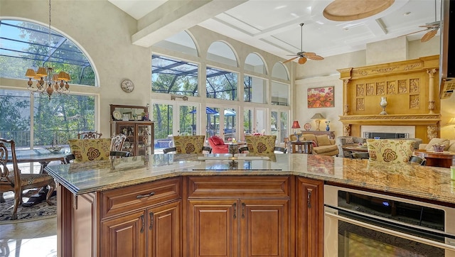 kitchen with coffered ceiling, a towering ceiling, ceiling fan with notable chandelier, light stone countertops, and stainless steel oven