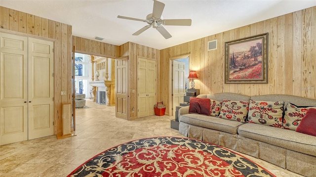 living room with ceiling fan, wooden walls, and light tile patterned floors