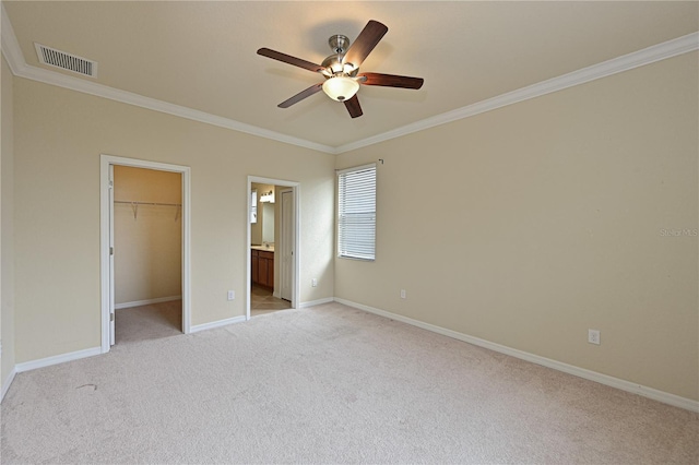 unfurnished bedroom featuring crown molding, light carpet, ceiling fan, and a walk in closet