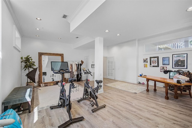 exercise room with ornamental molding and light hardwood / wood-style floors