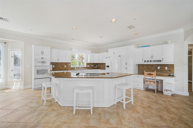 kitchen featuring white cabinets, white appliances, a kitchen bar, and a kitchen island