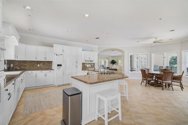 kitchen with white fridge with ice dispenser, a breakfast bar area, white cabinetry, decorative backsplash, and ceiling fan