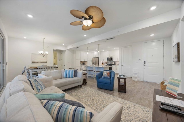 living room featuring light wood-type flooring and ceiling fan with notable chandelier